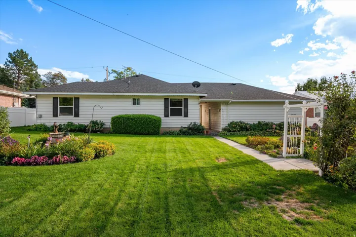 White horizontal siding exterior with dark shutters, dark shingle roof, green lawn, and established landscaping