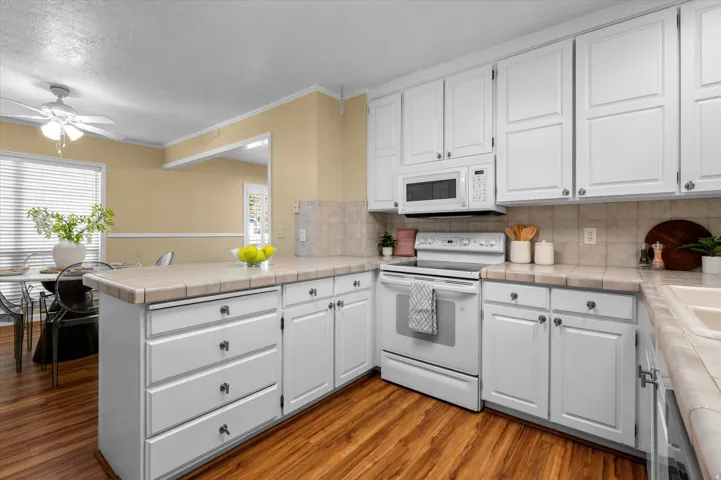Kitchen featuring white cabinetry, tile countertops, tile backsplash, built-in microwave, and wood-finish flooring