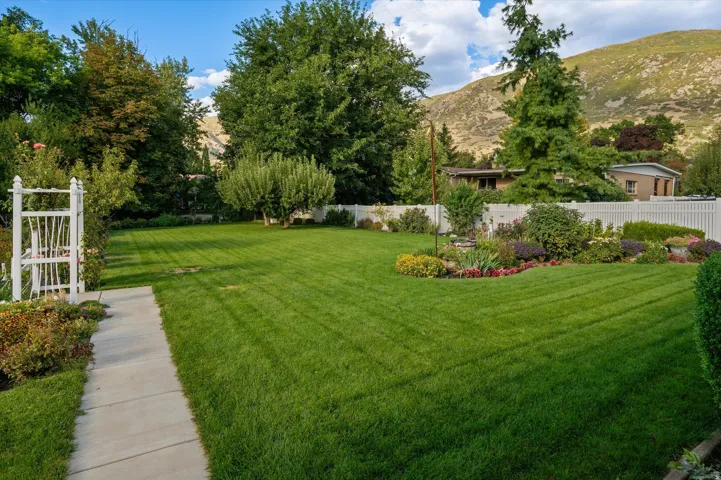 Expansive lawn space, established trees, concrete pathway, white privacy fencing, and mature landscaping