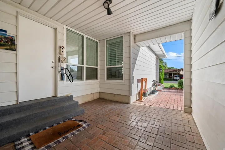 Covered entry with brick paver flooring, multiple windows, and exterior siding