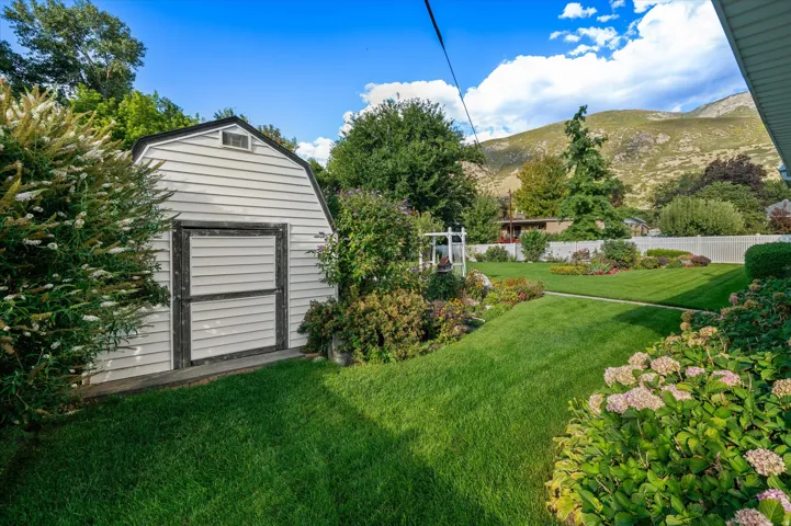 Expansive backyard featuring a manicured lawn, established landscaping, and a white picket fence