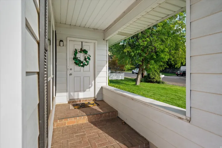 Covered front porch with brick paver flooring, paneled front door, and exterior sconce lighting