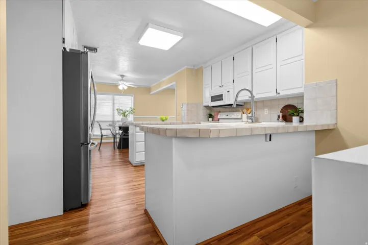 Wood-finish flooring throughout, white cabinetry with recessed panel doors, tile countertops, integrated sink with gooseneck faucet, and flush-mount ceiling lights