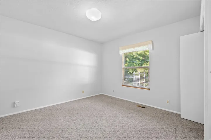 Neutral wall paint with textured carpet flooring, a window with horizontal blinds, and a flush mount ceiling light fixture
