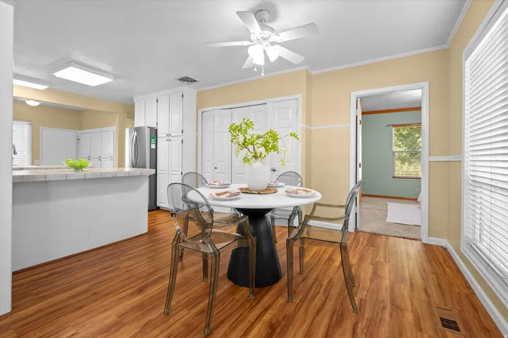 Wood-finish flooring, white ceiling fan, white paneled doors, white kitchen cabinetry, and a kitchen island with a light-colored countertop