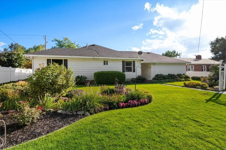 Expansive front yard featuring a manicured lawn, established landscaping, white vinyl fencing, and a well-maintained exterior