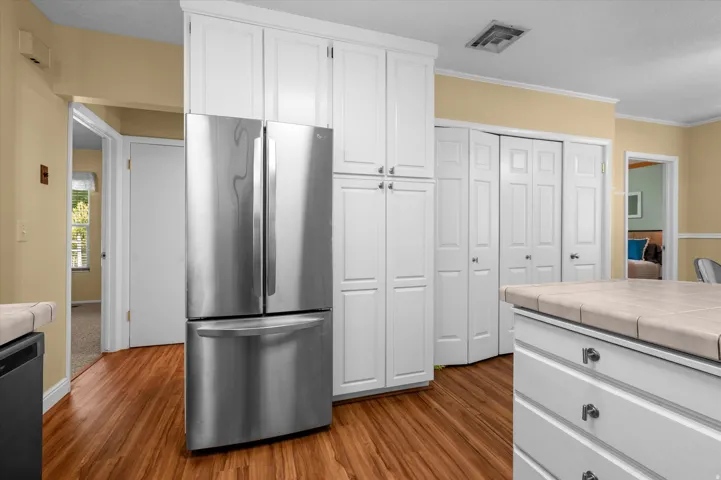 Stainless steel French door refrigerator, white shaker-style cabinetry, wood-finish flooring, tiled island countertop, and white bi-fold doors