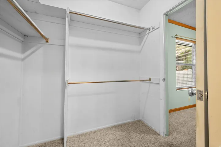 Open closet with multiple hanging rods and carpet flooring