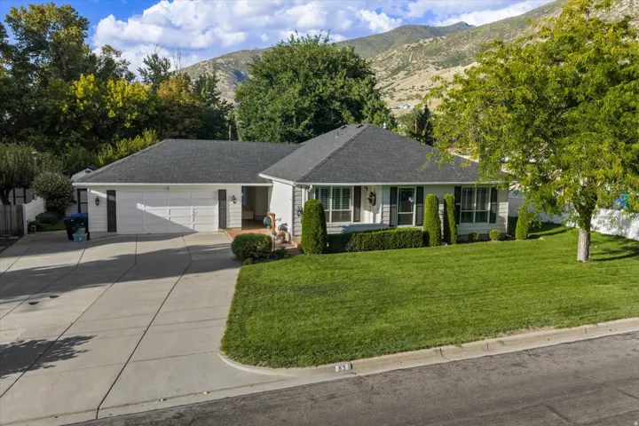 Exterior featuring a two-car garage, concrete driveway, front lawn, and mature trees