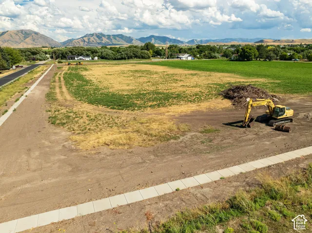 Expansive land parcel featuring established sidewalks, a paved road, and distant mountain scenery