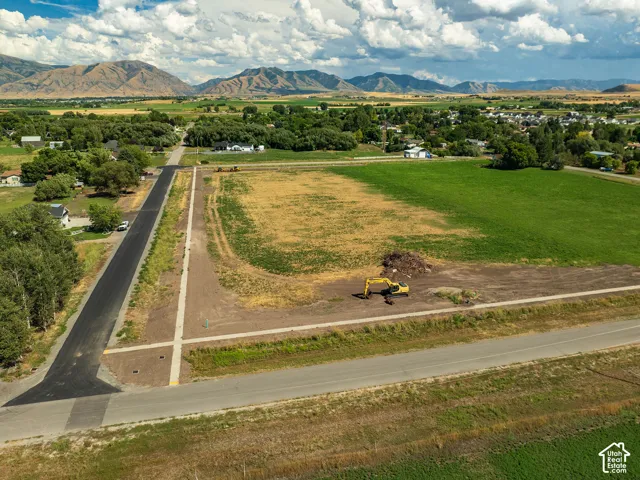 Expansive land parcel with surrounding agricultural fields, newly paved road access, and mountain backdrop