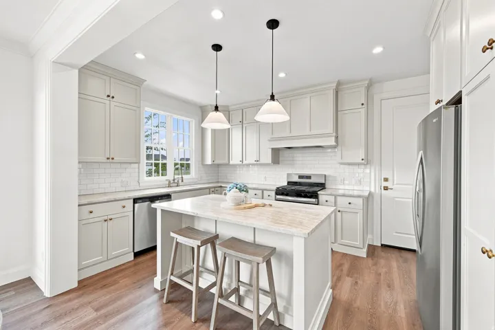 White shaker cabinetry, wood-finish flooring, undermount sink, stainless steel appliances, and a central island with pendulum lighting