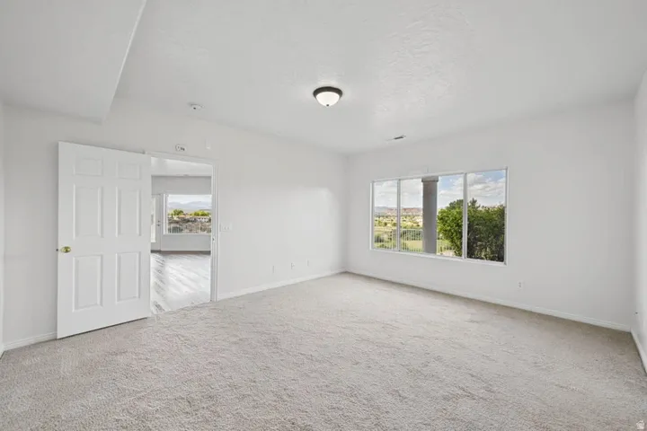 Carpeted room with a large window, a six-panel interior door, and a flush mount ceiling light