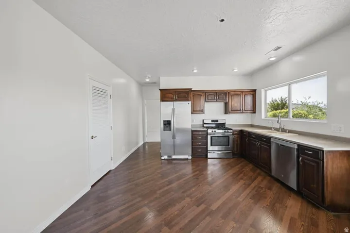 Kitchen featuring wood-finish flooring, dark wood cabinetry, stainless steel appliances, and a window over the sink