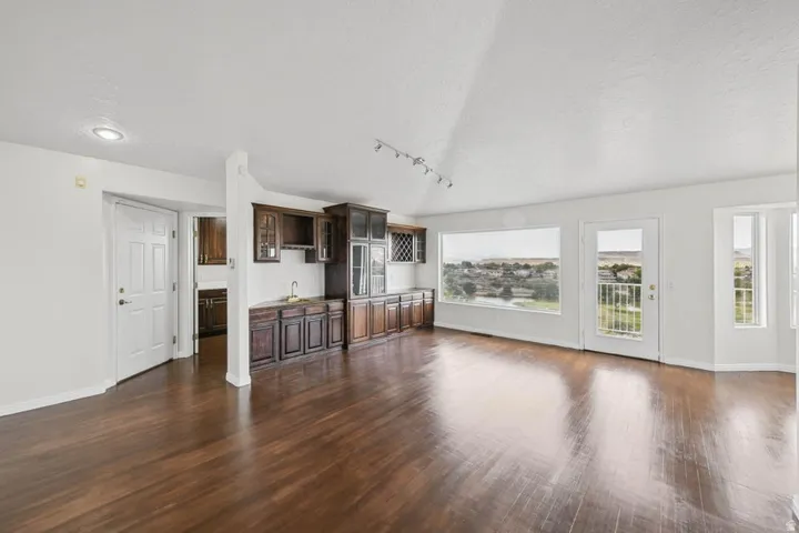 Hardwood-finish flooring, built-in wet bar with cabinetry, multiple windows, and exterior door with a balcony