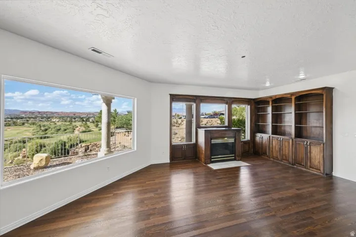 Dark wood-finish flooring, built-in shelving, built-in cabinetry, and a fireplace with a hearth
