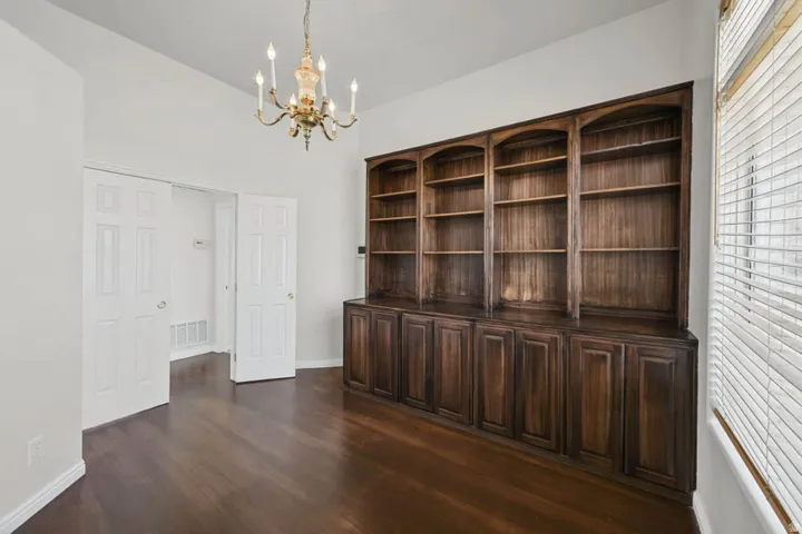 Built-in wood cabinetry with arched shelving, wood-finish flooring, and a brass chandelier