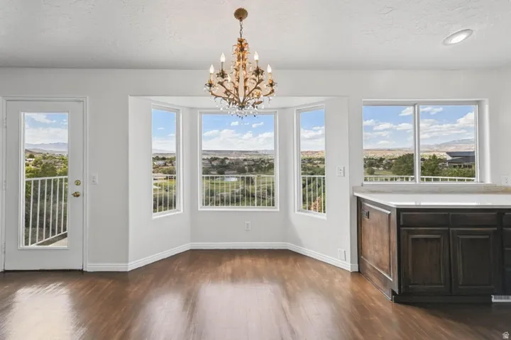 Bay window, wood-finish flooring, white walls, built-in cabinetry with light-colored countertop, decorative chandelier