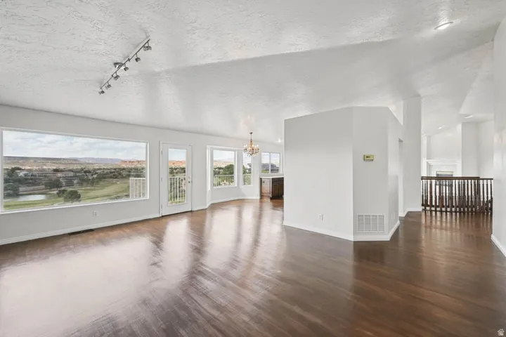 Expansive living area with wood-finish flooring, track lighting, and a panoramic window framing the distant landscape