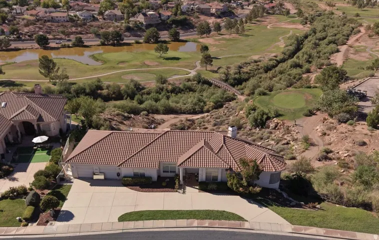 Tile roof, expansive paved driveway, manicured front landscaping, and a golf course with water features in the background