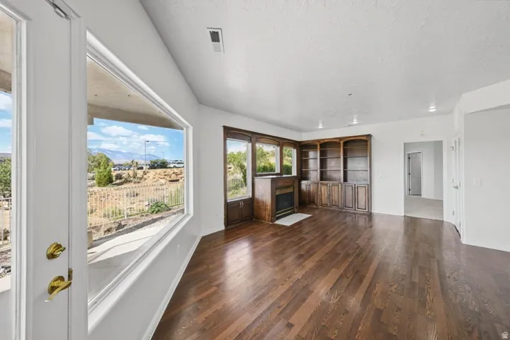 Expansive room with dark wood-finish flooring, corner fireplace with built-in cabinetry, and large windows