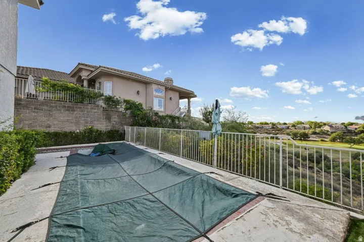 Outdoor pool with concrete decking, surrounded by a white metal fence and retaining wall