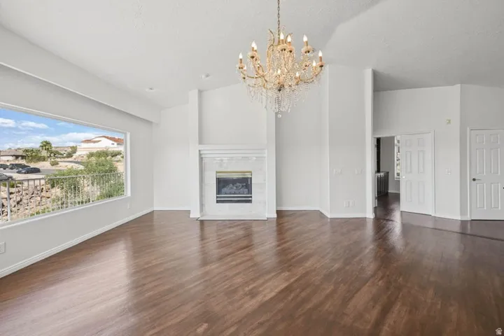 Expansive living space featuring wood-finish flooring, a decorative chandelier, and a fireplace with a white mantel