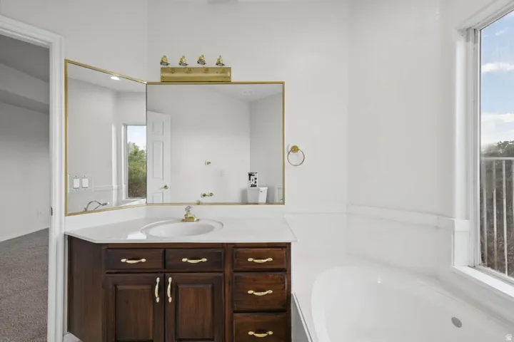 Built-in wood vanity with a white countertop and integrated sink, a large wall-mounted mirror, a four-bulb vanity light fixture, and an integrated soaking tub