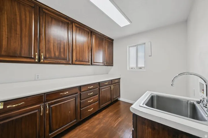 Extensive wood-finish cabinetry with brass hardware, white countertops, stainless steel sink with chrome faucet, and wood-finish flooring