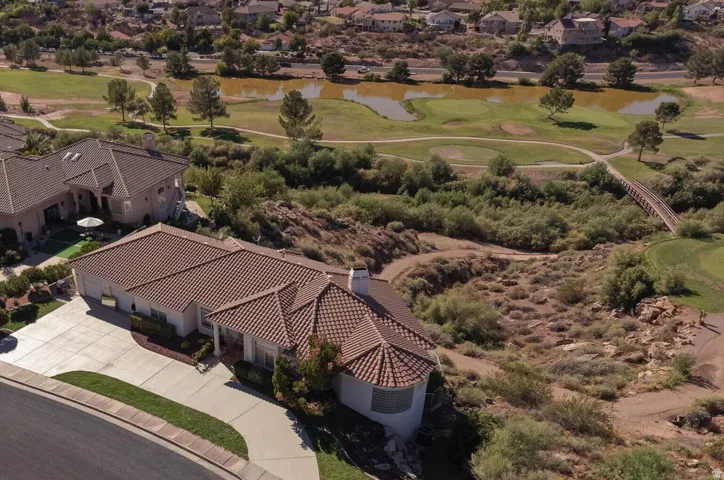 Tile roof structure, concrete driveway, lush landscaping, adjacent golf course, and natural terrain