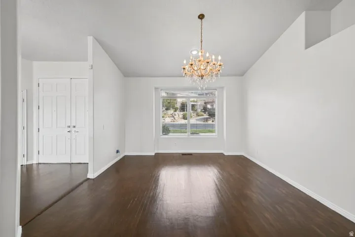 Vaulted ceiling with an ornate chandelier, wood-finish flooring, and a large window