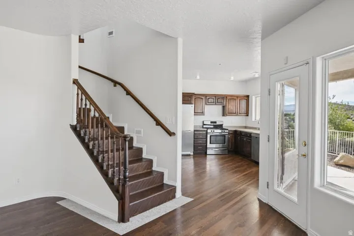 Hardwood flooring, dark wood cabinetry, stainless steel appliances, and a wood staircase with balusters