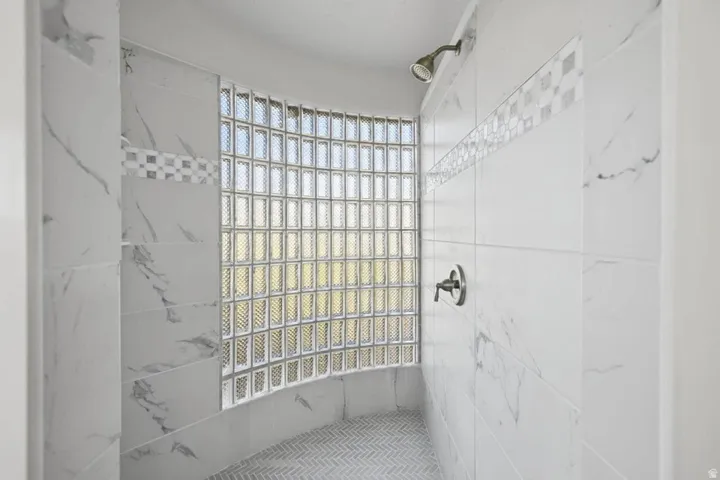 Curved glass block wall, full height marble-look tile, decorative mosaic tile accent, herringbone pattern shower pan, and dark bronze shower fixtures