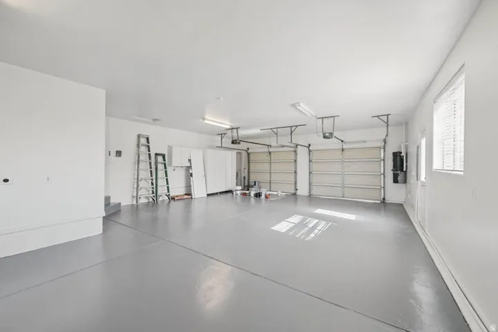 Attached two-car garage featuring a gray epoxy floor finish, multiple overhead light fixtures, and a side window with blinds