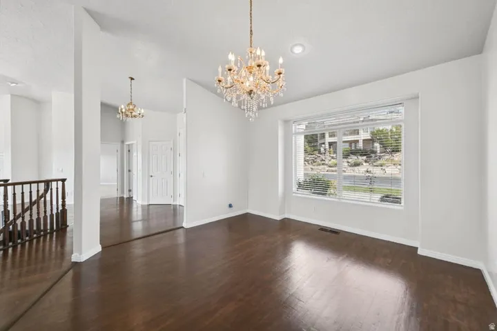 Elegant primary living space showcasing rich wood-finish flooring, soaring ceiling height with crown molding, and dual crystal chandeliers