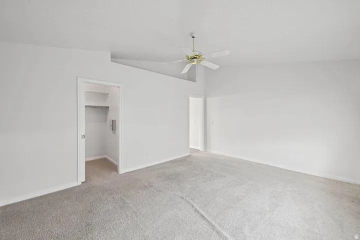 Spacious room featuring vaulted ceilings, ceiling fan, plush carpet flooring, and a walk-in closet with shelving