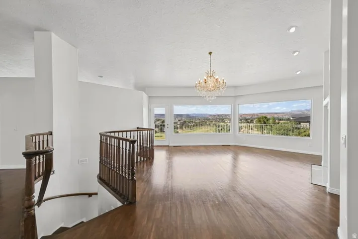 Spacious room featuring wood-finish flooring, a crystal chandelier, recessed lighting, and expansive windows