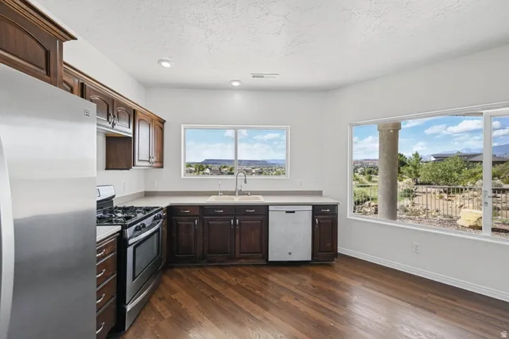 Wood-finish flooring, dark wood cabinetry, stainless steel appliances, light-toned countertops, and expansive windows