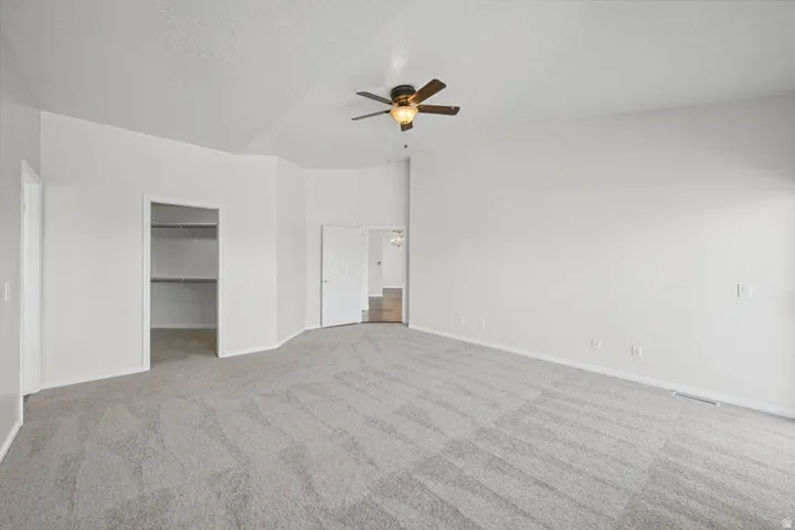 Vaulted ceiling with a ceiling fan, light gray carpeting, crisp white walls, and an open closet with built-in shelving