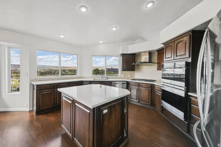 Kitchen featuring dark wood cabinetry, white countertops, a central island, recessed lighting, and stainless steel appliances including a built-in oven and microwave