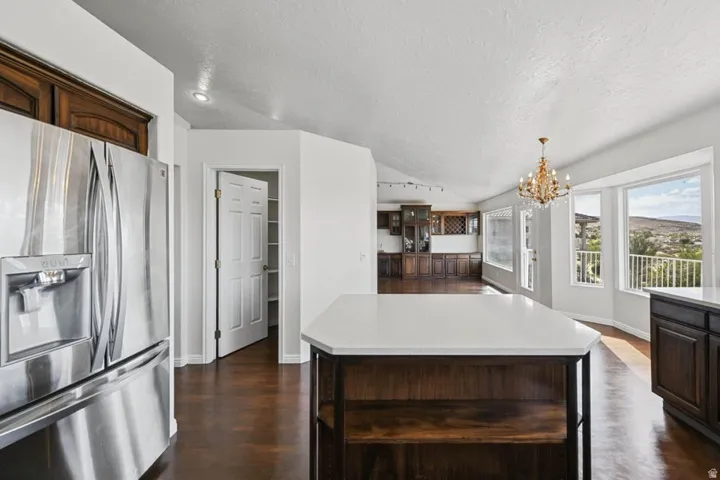 Stainless steel refrigerator with built-in ice and water dispenser, wood-finish flooring, white countertops, built-in cabinetry with wine rack, and a decorative chandelier