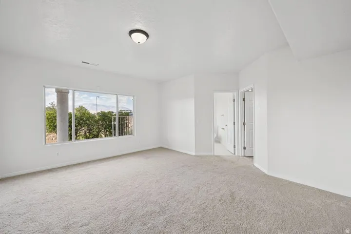 Expansive room featuring light-colored carpeting, white wall finishes, a large window offering natural light, and a flush-mount ceiling light fixture