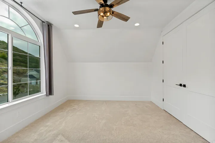 Arched picture window, recessed lighting, ceiling fan with wood-finish blades, soft carpet flooring, and white paneled doors with matte black hardware