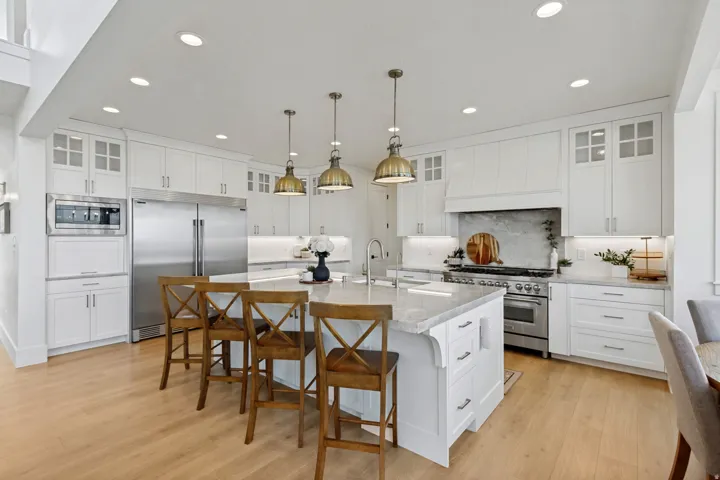 White cabinetry with glass-front accents, stainless steel appliances, a large island with integrated sink, and recessed lighting