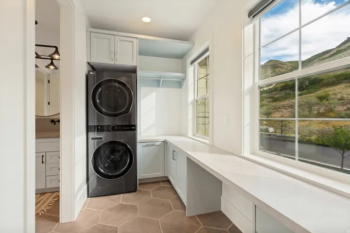 Hexagonal tile flooring, stacked laundry appliances, light-toned cabinetry, built-in countertop, and multiple large windows