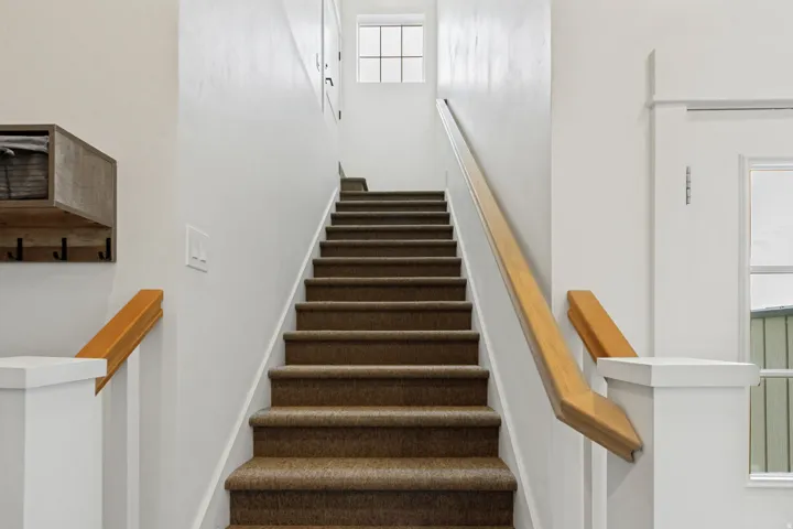 Staircase featuring carpeted treads, wood handrails, and white painted newel posts