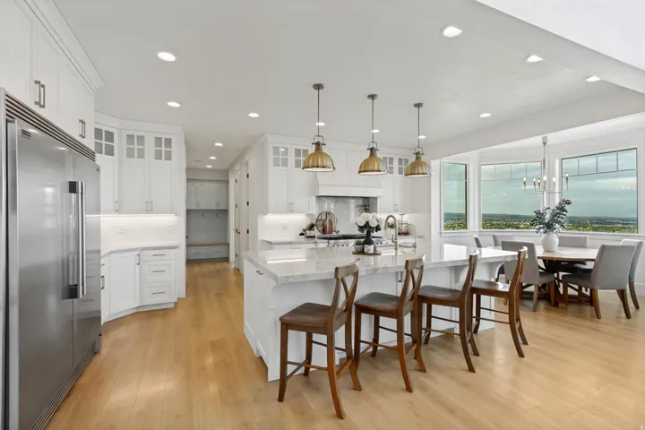 Gourmet kitchen with stainless steel refrigerator, white cabinetry, a large kitchen island with counter seating, and wood-finish flooring throughout