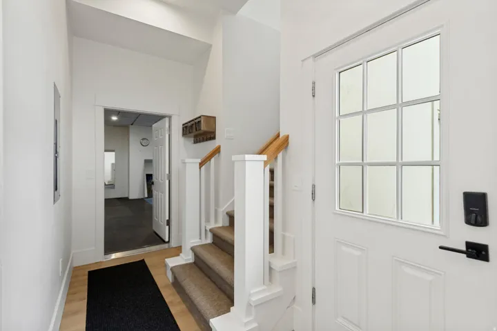 Entryway featuring a white paneled door with grid-patterned glass, light wood-finish flooring, a carpeted staircase with white risers and wood handrails, and white walls