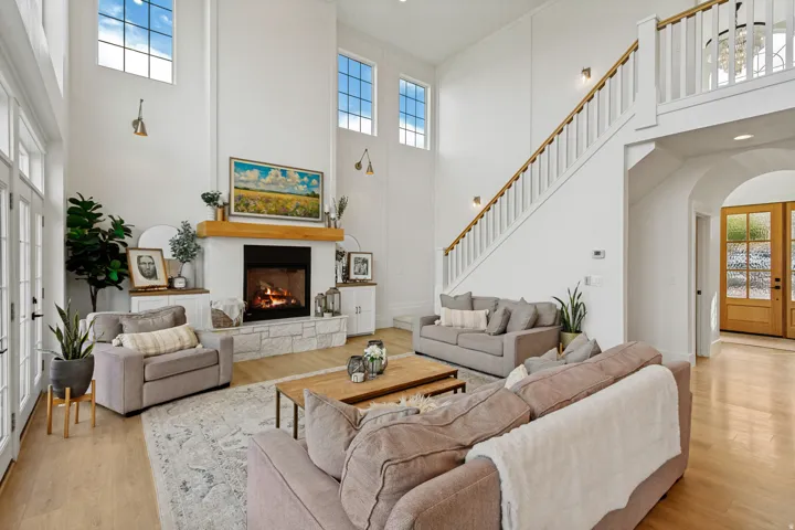 Spacious living area featuring a tall ceiling, a stone-faced fireplace with wood mantel, and multiple large windows