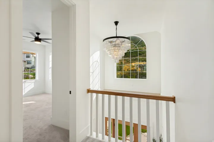 Arched window, tiered chandelier, white baluster railing with wood-finish top rail, white walls, and carpet flooring